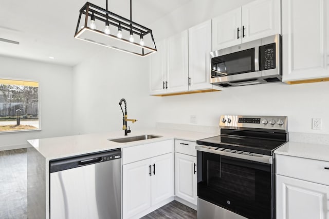 kitchen featuring stainless steel appliances, a peninsula, a sink, white cabinetry, and dark wood-style floors