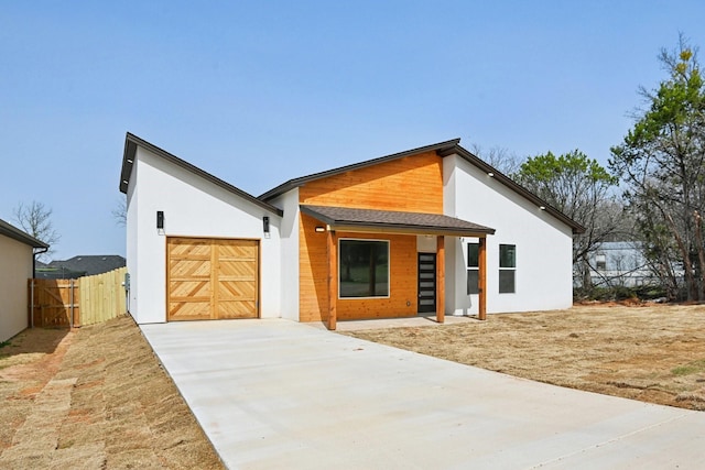 modern home featuring an attached garage, driveway, fence, and stucco siding