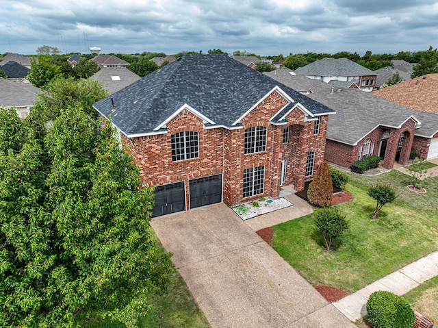 traditional home with driveway, roof with shingles, an attached garage, a front lawn, and brick siding