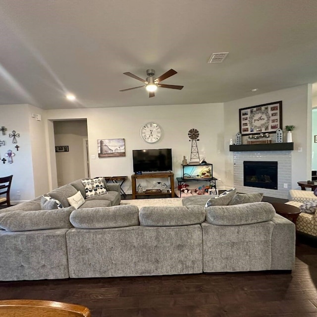 living room featuring a brick fireplace, ceiling fan, visible vents, and dark wood finished floors