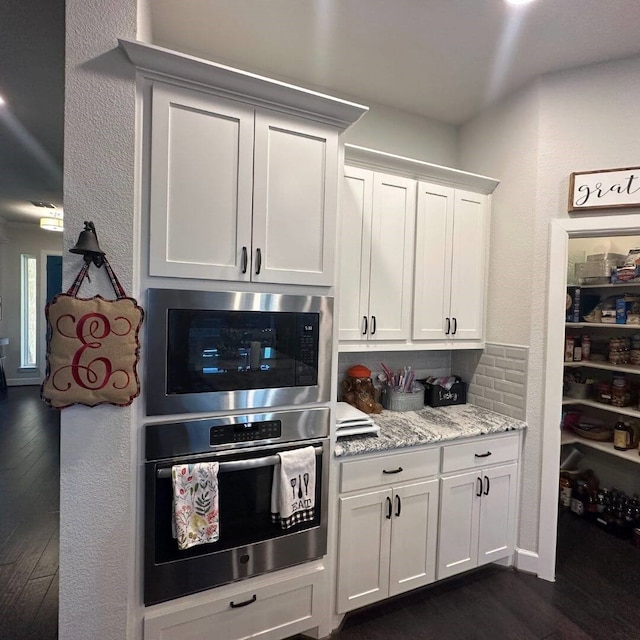 kitchen featuring light stone counters, dark wood-type flooring, stainless steel oven, built in microwave, and white cabinetry