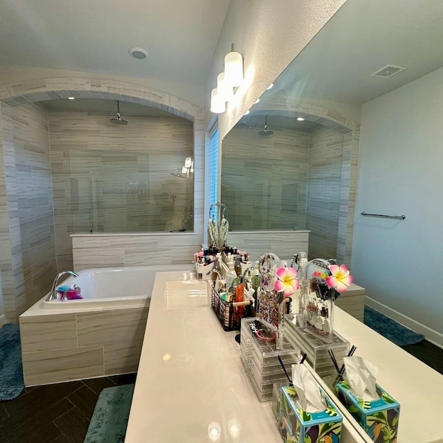 full bath with a washtub, visible vents, baseboards, tiled shower, and double vanity