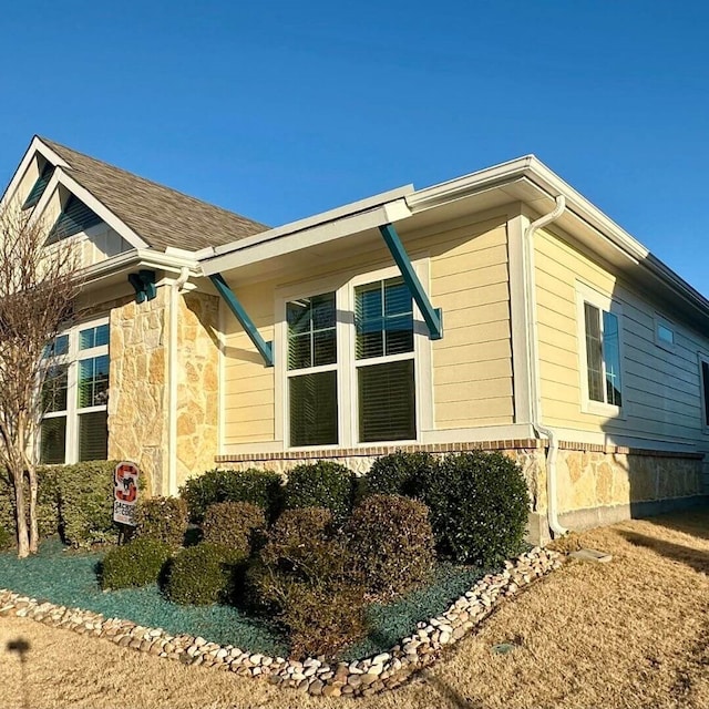 view of side of property featuring a shingled roof and stone siding