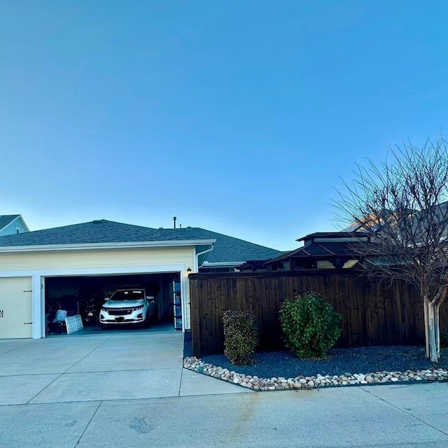 view of side of property with a garage, concrete driveway, roof with shingles, and fence