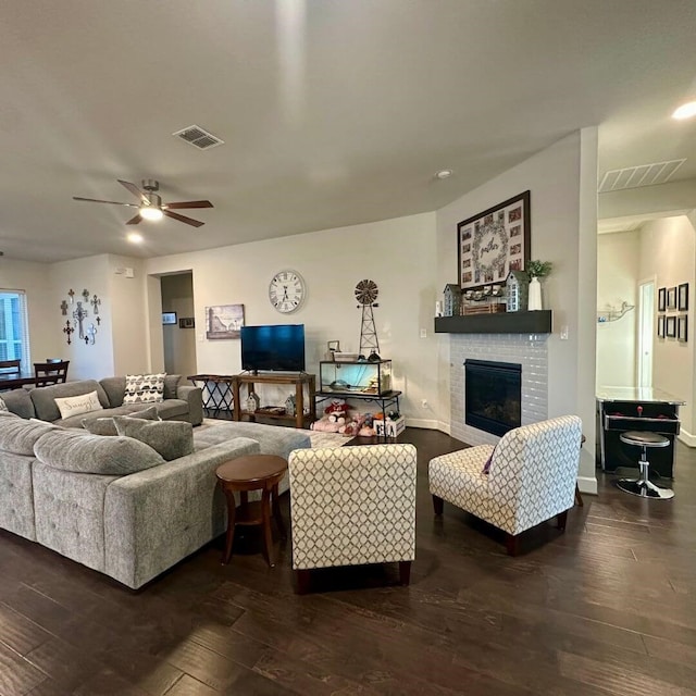 living room with a ceiling fan, a glass covered fireplace, visible vents, and wood finished floors