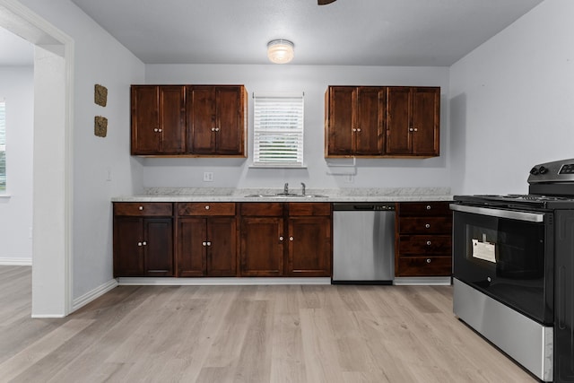 kitchen featuring light wood finished floors, stainless steel appliances, a sink, dark brown cabinets, and baseboards