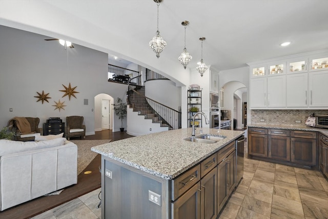 kitchen featuring backsplash, glass insert cabinets, arched walkways, white cabinetry, and a sink