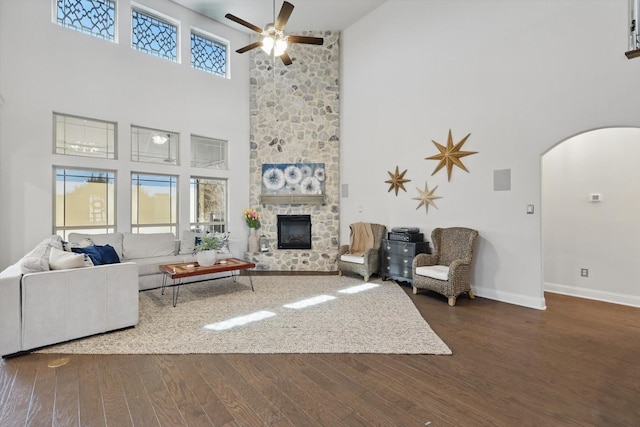 living room with wood finished floors, baseboards, arched walkways, ceiling fan, and a stone fireplace