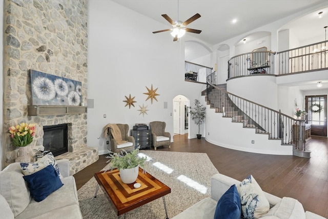 living room with wood finished floors, baseboards, arched walkways, a stone fireplace, and stairs