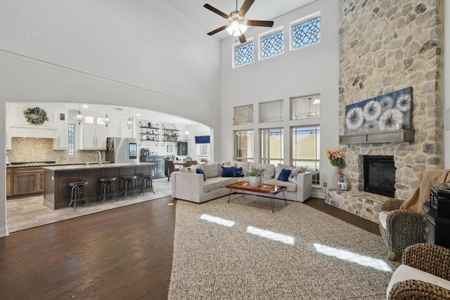 living room featuring arched walkways, ceiling fan, a fireplace, and light wood-style floors