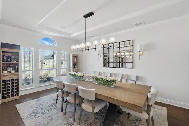 dining space featuring wood finished floors, baseboards, visible vents, a tray ceiling, and crown molding