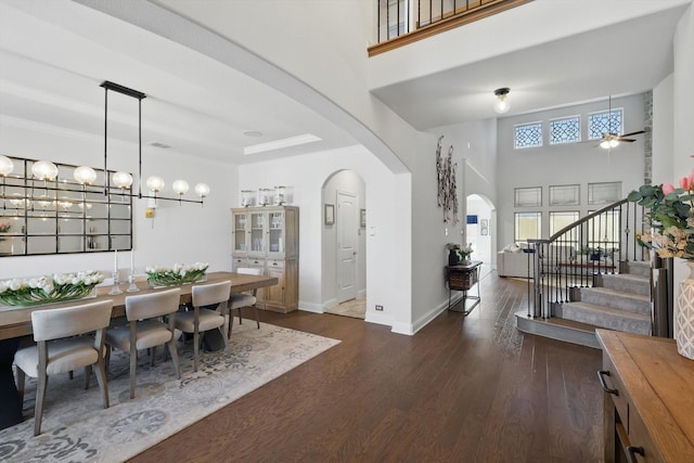 entryway featuring baseboards, arched walkways, stairs, dark wood-style floors, and a ceiling fan