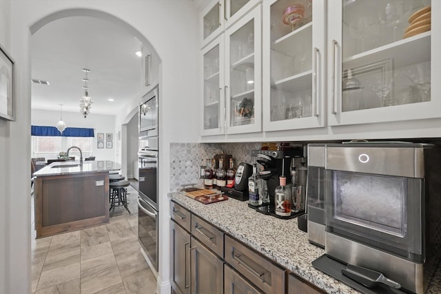 bar featuring visible vents, a sink, stainless steel microwave, tasteful backsplash, and arched walkways