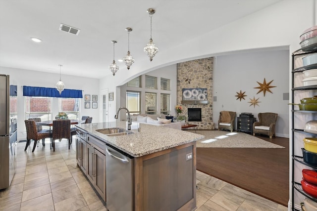 kitchen with visible vents, a sink, stainless steel dishwasher, a stone fireplace, and light stone countertops