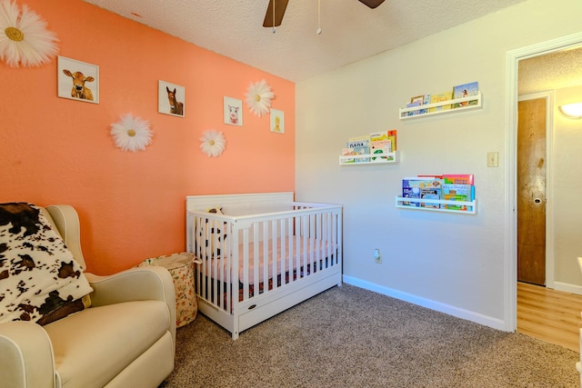 bedroom featuring carpet, a crib, baseboards, and a textured ceiling