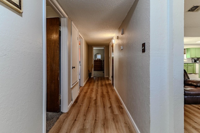 hallway featuring a textured ceiling, a textured wall, visible vents, light wood-style floors, and baseboards