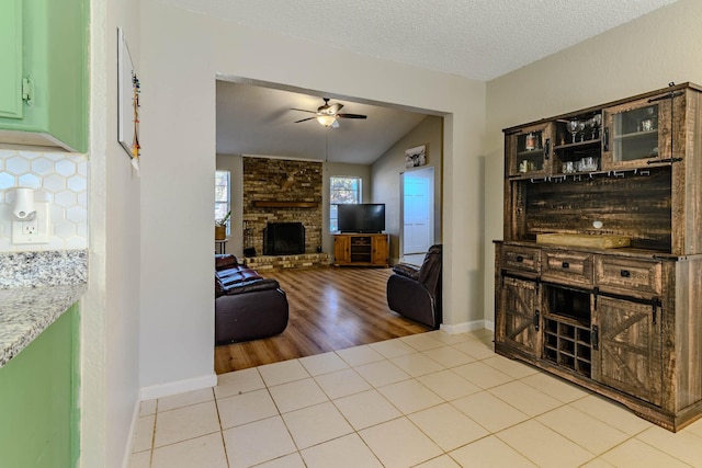 living area with a ceiling fan, a large fireplace, a textured ceiling, and tile patterned floors