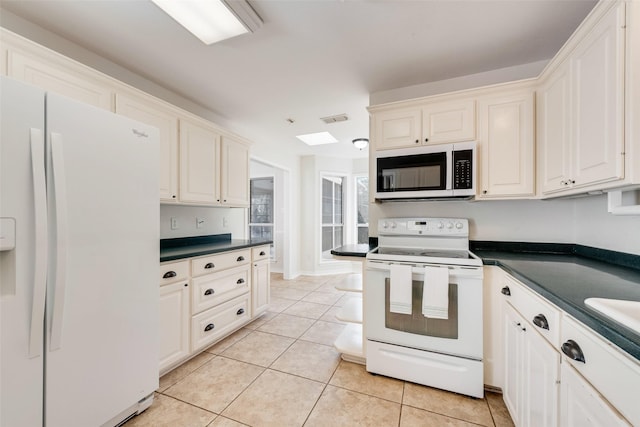 kitchen with dark countertops, white appliances, light tile patterned floors, and visible vents