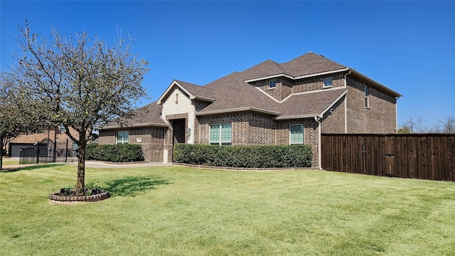 view of front of home with a front lawn, fence, brick siding, and roof with shingles