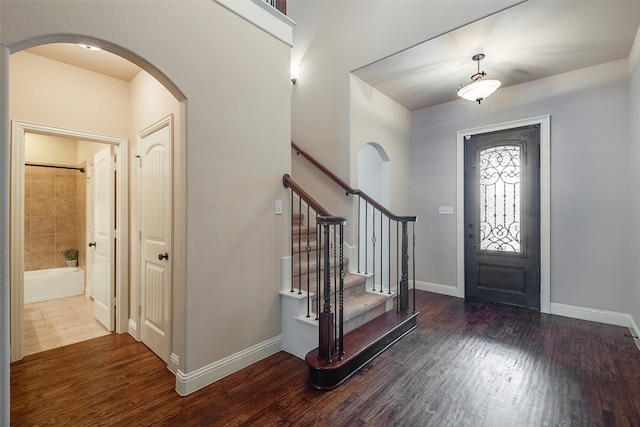 foyer entrance featuring arched walkways, wood finished floors, stairs, and baseboards