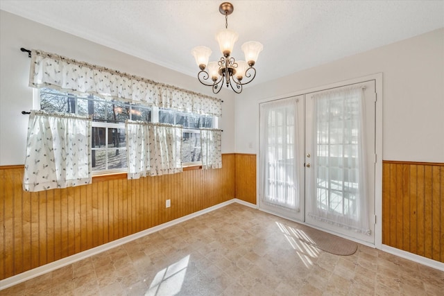 unfurnished dining area featuring a chandelier, french doors, a wainscoted wall, and wood walls