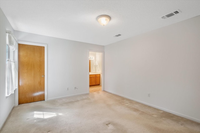 unfurnished bedroom featuring visible vents, connected bathroom, light carpet, and baseboards