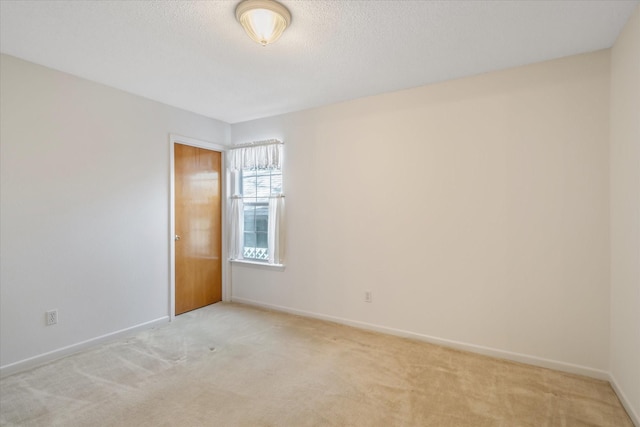 spare room with light carpet, a textured ceiling, and baseboards