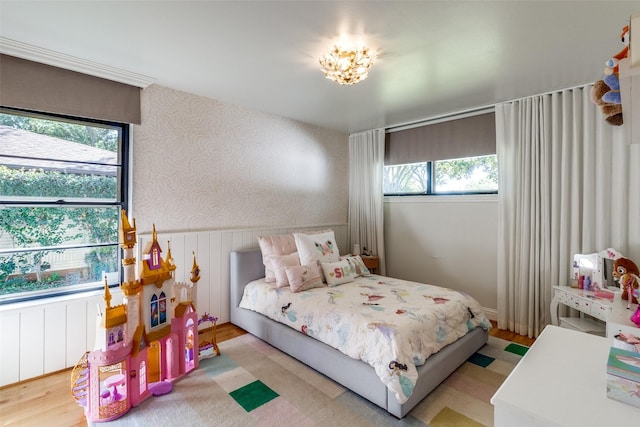 bedroom with wallpapered walls, wood finished floors, and wainscoting