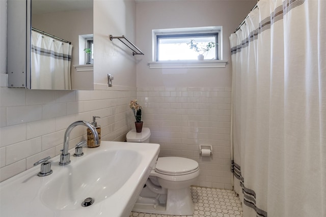 bathroom with a wainscoted wall, tile walls, toilet, a sink, and tile patterned floors