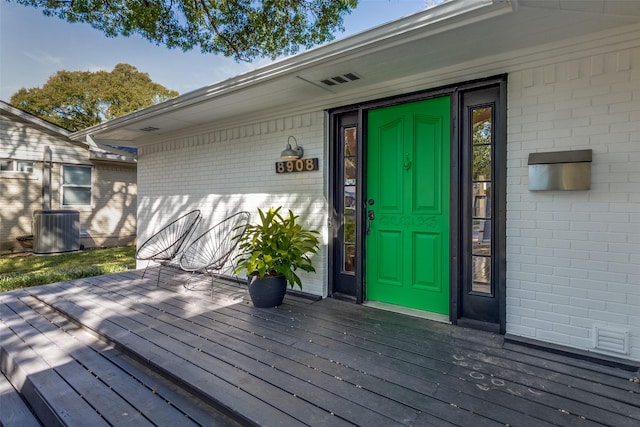 entrance to property featuring cooling unit, brick siding, and a deck