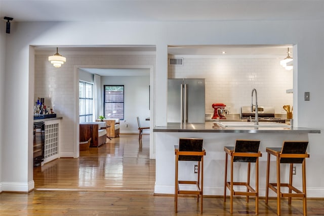 kitchen featuring a breakfast bar area, visible vents, backsplash, freestanding refrigerator, and wood-type flooring