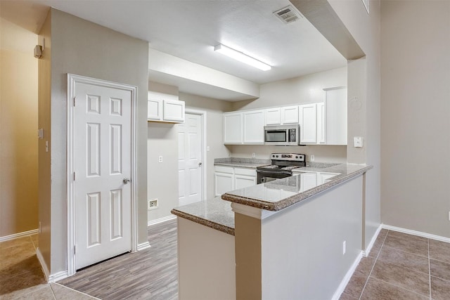 kitchen with light stone counters, a peninsula, visible vents, white cabinets, and appliances with stainless steel finishes