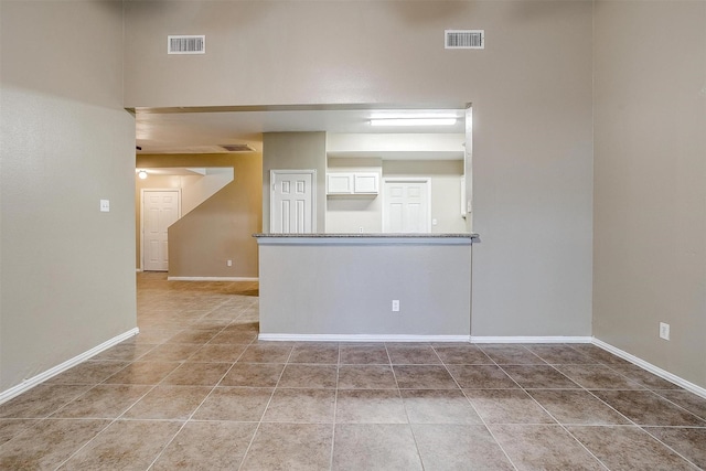 tiled spare room featuring baseboards and visible vents