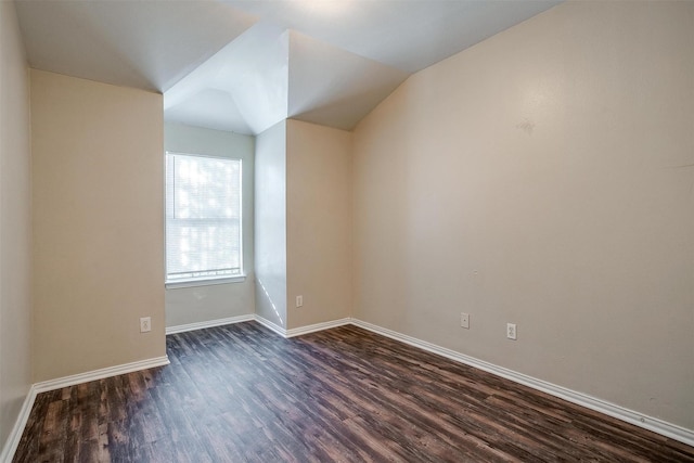 empty room with dark wood-type flooring, vaulted ceiling, and baseboards