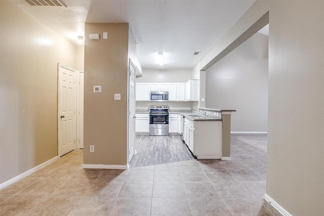 kitchen with light tile patterned floors, baseboards, stainless steel appliances, white cabinetry, and a sink