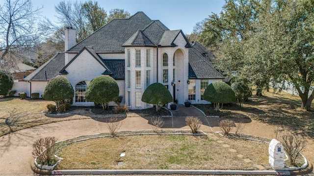 french provincial home featuring stone siding, driveway, and a chimney