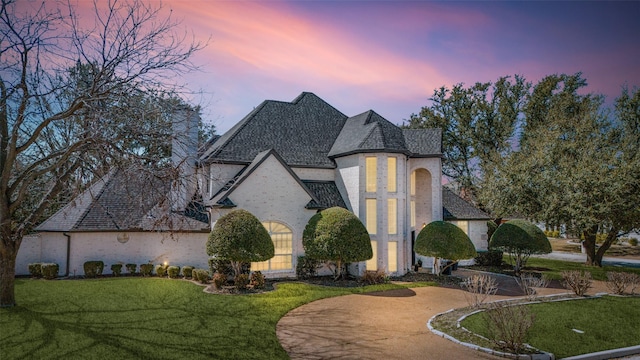 french country inspired facade featuring brick siding, concrete driveway, and a front lawn