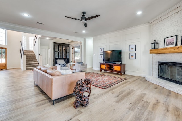 living room featuring visible vents, light wood finished floors, ceiling fan, stairs, and crown molding