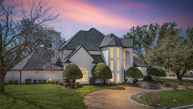 french provincial home featuring brick siding, curved driveway, and a front yard