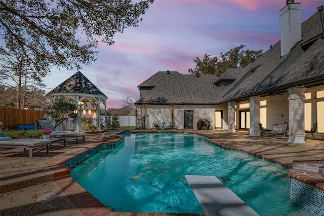 pool at dusk featuring a fenced in pool, a diving board, a patio, and fence