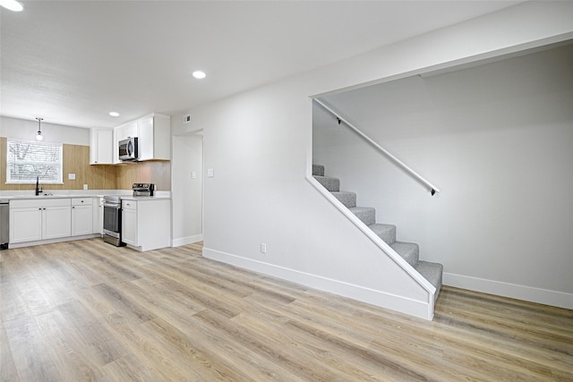 kitchen with a sink, white cabinets, light countertops, appliances with stainless steel finishes, and light wood finished floors