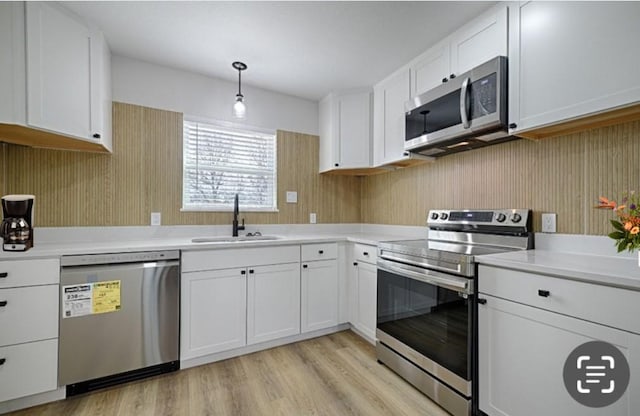 kitchen with stainless steel appliances, light countertops, white cabinets, a sink, and light wood-type flooring