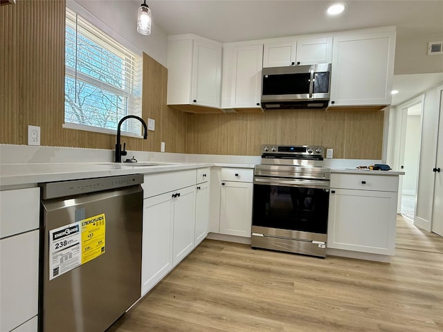 kitchen with stainless steel appliances, a sink, white cabinetry, light countertops, and light wood finished floors