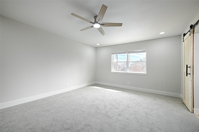 unfurnished bedroom featuring ceiling fan, a barn door, recessed lighting, carpet flooring, and baseboards