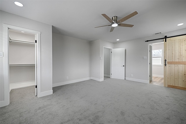 unfurnished bedroom featuring a barn door, visible vents, carpet, a spacious closet, and recessed lighting