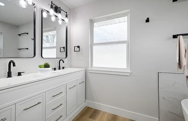 full bathroom with double vanity, wood finished floors, a sink, and baseboards