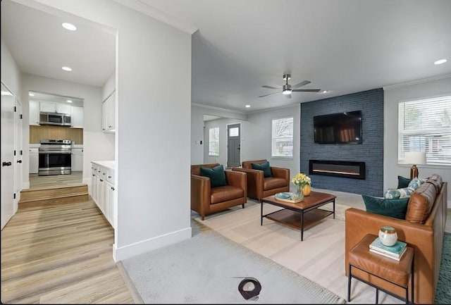 living room with plenty of natural light, ornamental molding, a fireplace, and light wood-style flooring