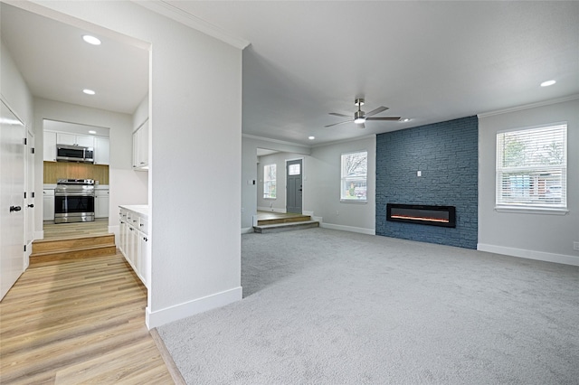 living area with a large fireplace, ceiling fan, baseboards, and crown molding