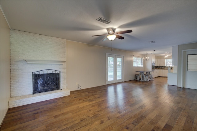 unfurnished living room featuring visible vents, dark wood-style floors, french doors, a fireplace, and ceiling fan with notable chandelier