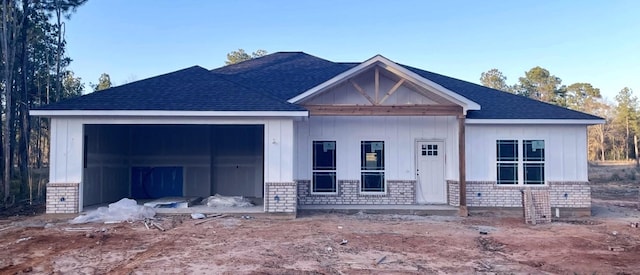 view of front of home with an attached garage, covered porch, brick siding, a shingled roof, and board and batten siding